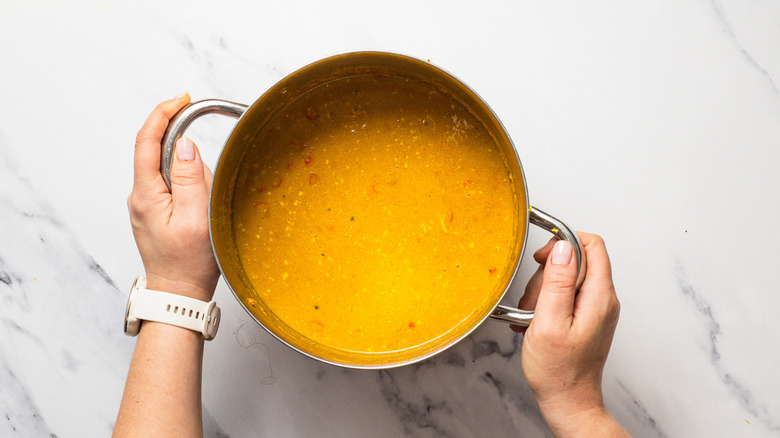 Hands holding pot of seasoned yellow curry chicken soup.