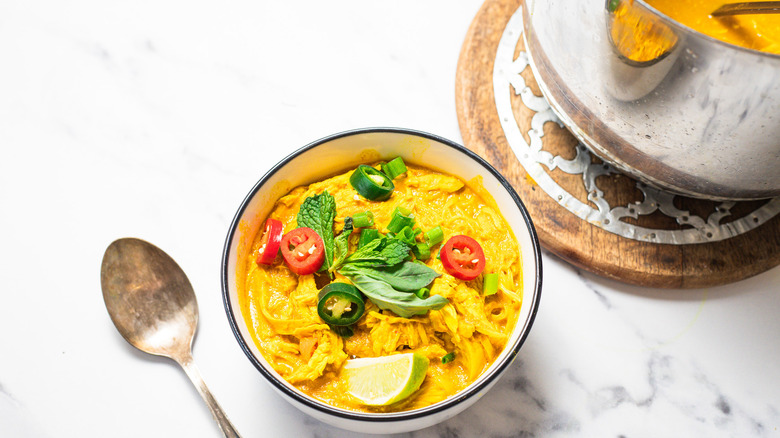 One bowl of coconut curry chicken noodle soup with large pot beside it.