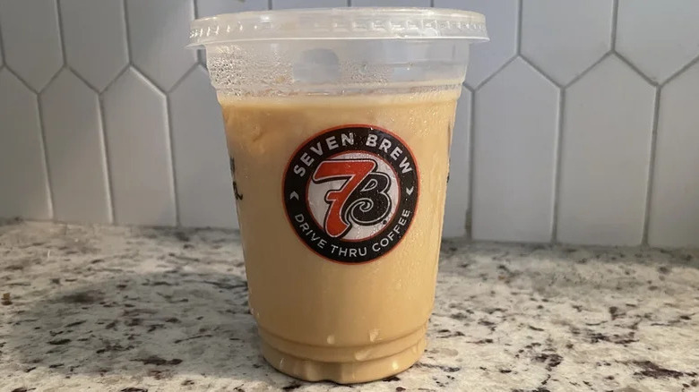 A vanilla latte in a branded plastic cup from 7 Brew, sitting on a marbled surface against a white tiled background