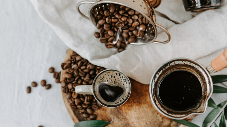 A cup of strong coffee on a tray next to whole beans and a stovetop coffee pot