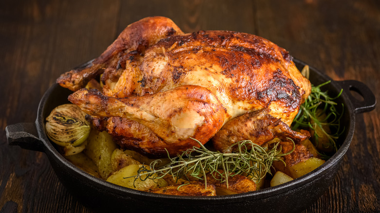 A roasted chicken in a cast iron pan atop brussels sprouts and potatoes