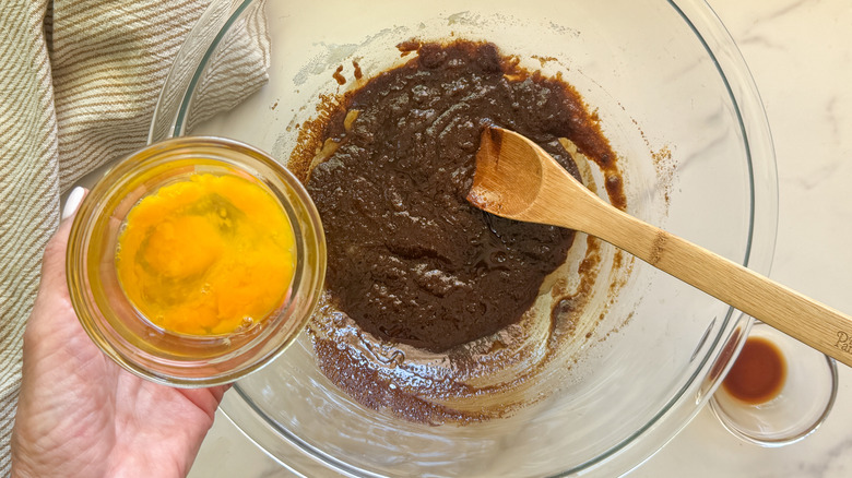 hand adding egg to bowl with dark coffee mixture