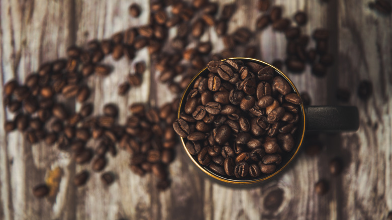 Aerial view of espresso beans in a mug and scattered on a wooden surface