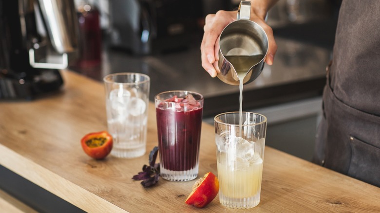 Hand pouring three cocktails on a bar top