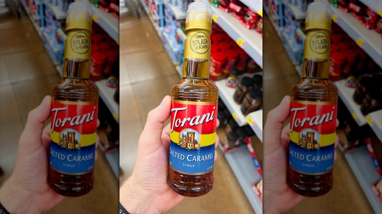 Hand holding Torani salted caramel coffee syrup bottle in store aisle