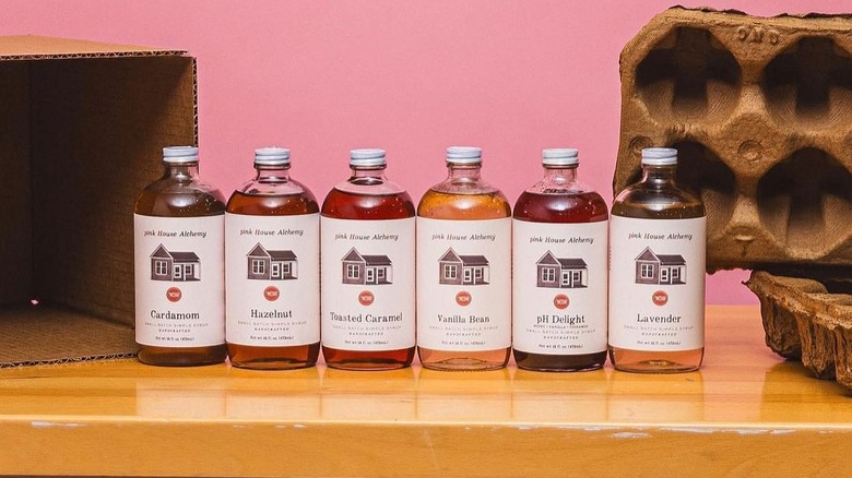 Pink House Alchemy coffee syrup bottles lined up with cartons