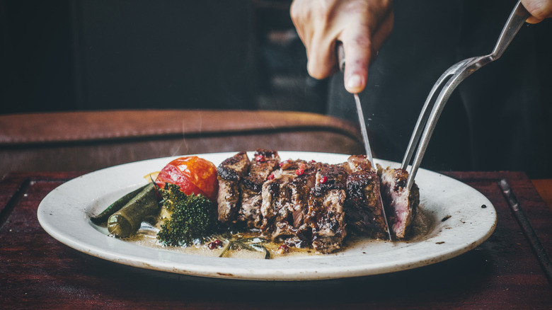 A steak on a plate with vegetables being cut