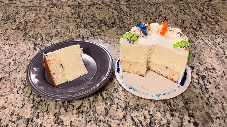 A slice of Baskin-Robbins' Celebration Party Cake sits on a purple plate on the left while the rest of the cake sits on a white plate on the right
