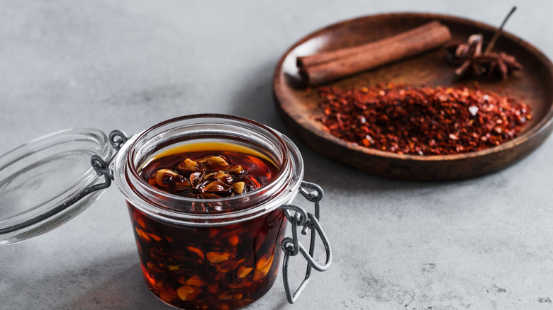 Swing-top jar of chili crisp with a wooden dish of spices in the background