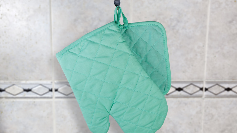 Teal oven mitt and potholder hanging off a black Command Hook