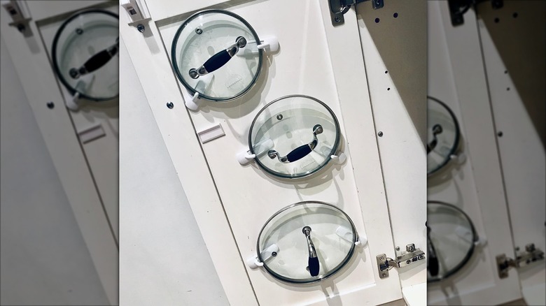 Two pot lids being held up by Command hooks on the inside of a cupboard