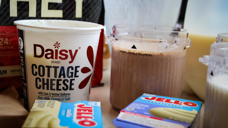 Whey protein, cottage cheese, and Jello boxes on table alongside Ninja CREAMi containers