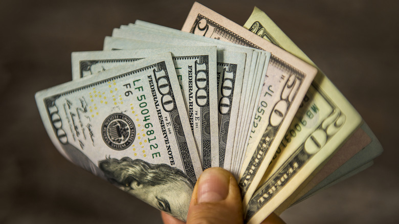 Hand holding fan of dollar bills in increments of 20, 50, and 100