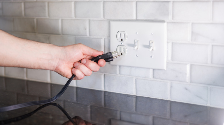 Hand plugging cord into power outlet in kitchen