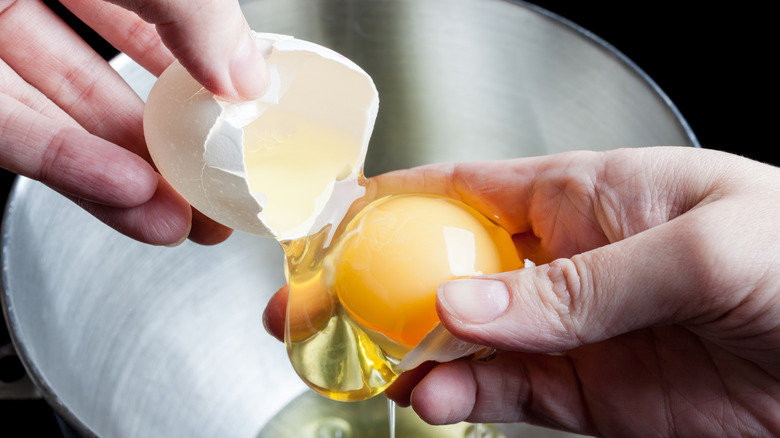 CLose up of hands using an eggshell to separate yolks from whites.