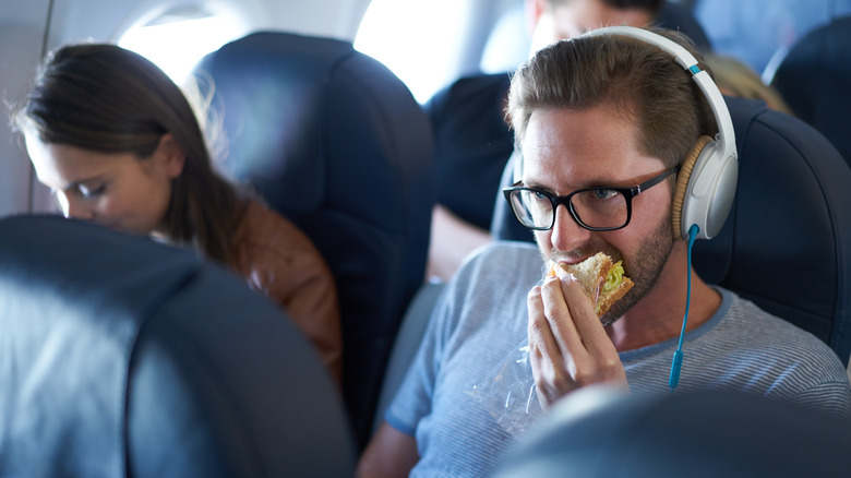 guy with headphones eats sandwich on plane