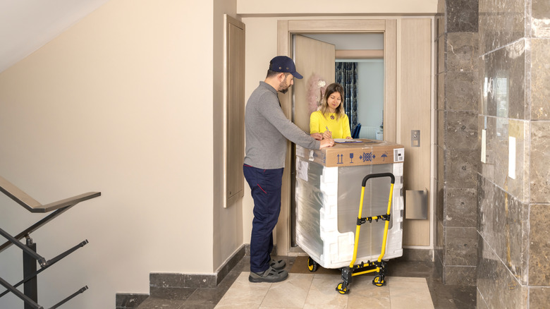 Man delivering a new appliance, still in its shipping packaging, to a woman's apartment