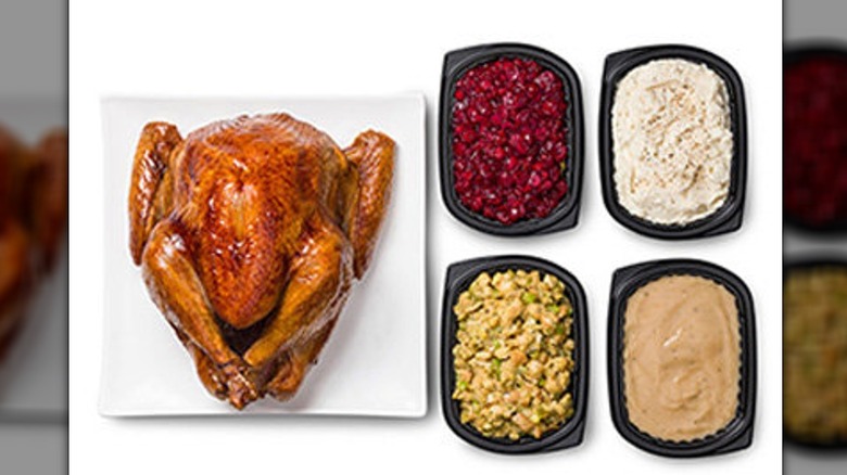 A turkey on a platter with sides in black containers