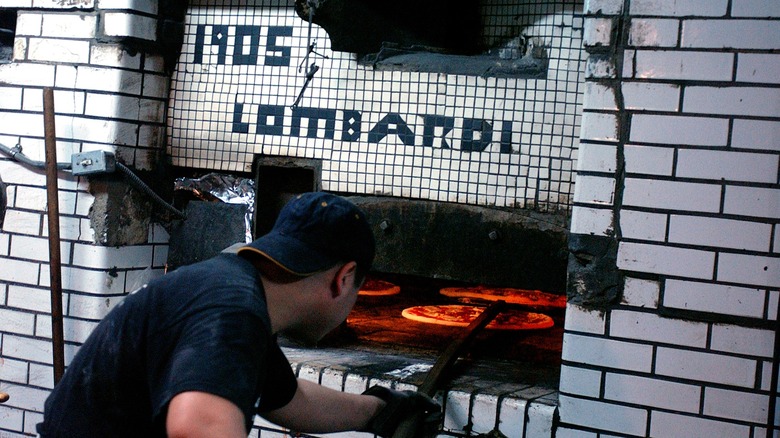 A person working with a brick pizza oven that has the words 1905 Lombardi on the front