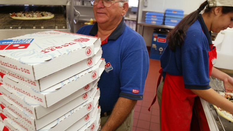 Workers prepare pizza and carry boxes in a Dominos Pizza