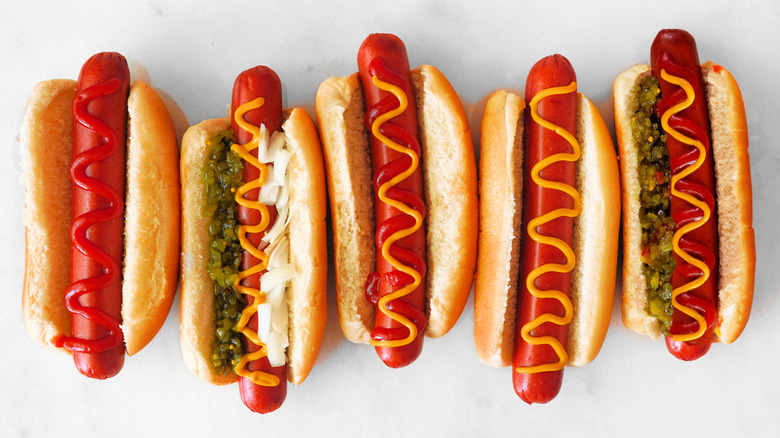 Five hot dogs with various toppings in buns alongside one another