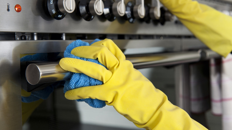Yellow gloved hands cleaning a stainless steel oven