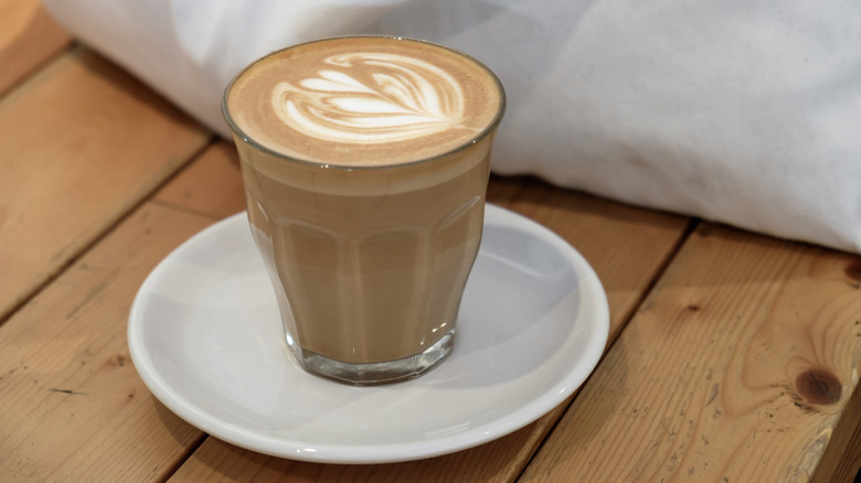 A Duralex Le Picardie tumbler filled with a latte on a white plate