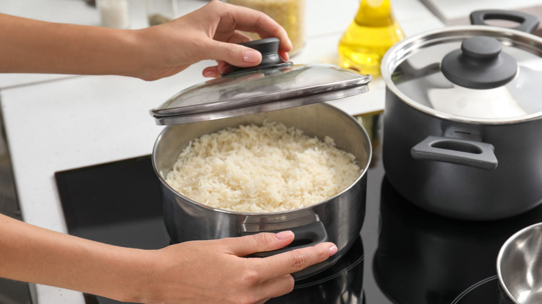 Close-up of hands adjusting a pot of rice cooking on a stove