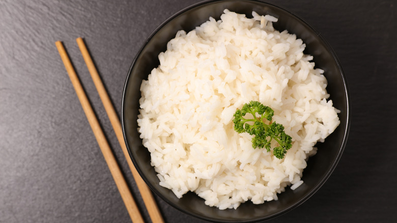 A black bowl of cooked white rice next to a pair of chopsticks