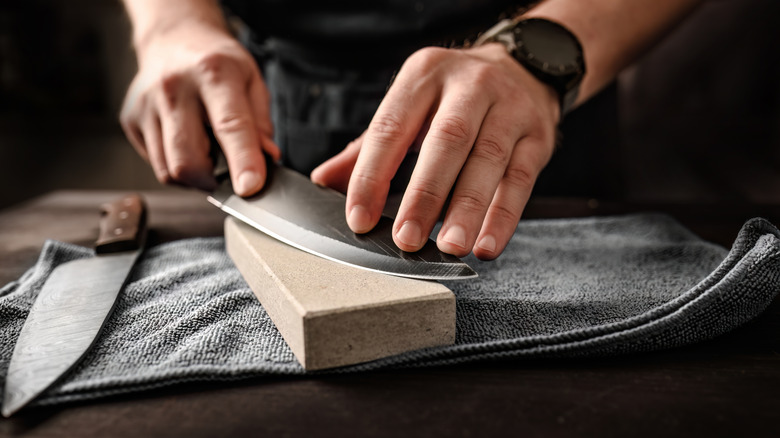 Two hands manually sharpening a knife on a wet stone