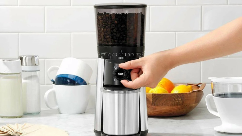 A person's hand adjusting the dial on an Oxo coffee grinder.