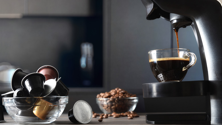 K-cup coffee maker dispensing coffee with bowl of coffee pods nearby
