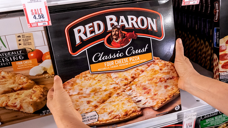 Someone holding up a Red Baron Classic Crus Four Cheese pizza box