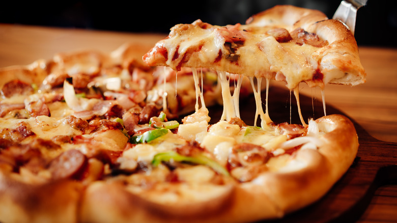 A slice of frozen pizza being lifted from the whole baked, gooey pie
