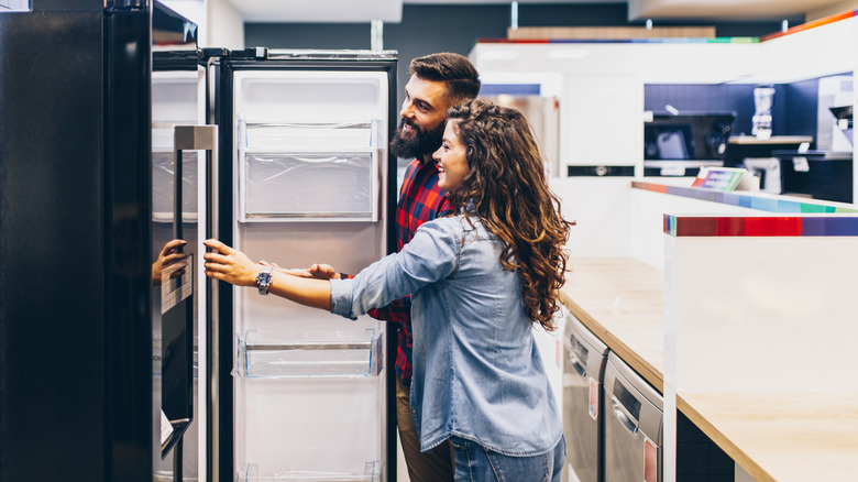 A man and a woman looking into the inside of a fridge that's displayed in a store.