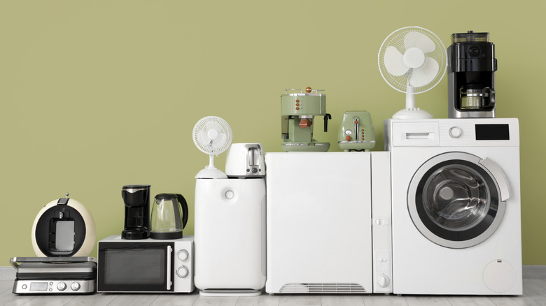 White home appliances including laundry machine, mini refrigerator, coffee maker, and microwave against sage green wall
