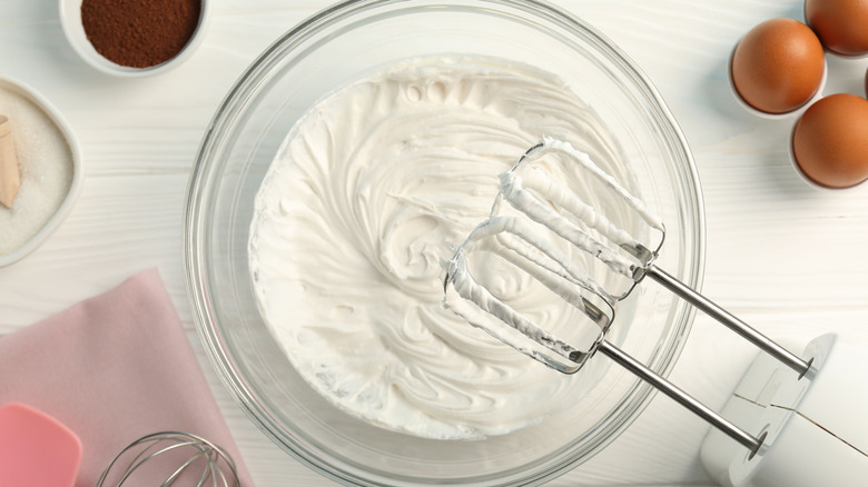 Top view of whipped egg whites with the hand mixer resting above the bowl.