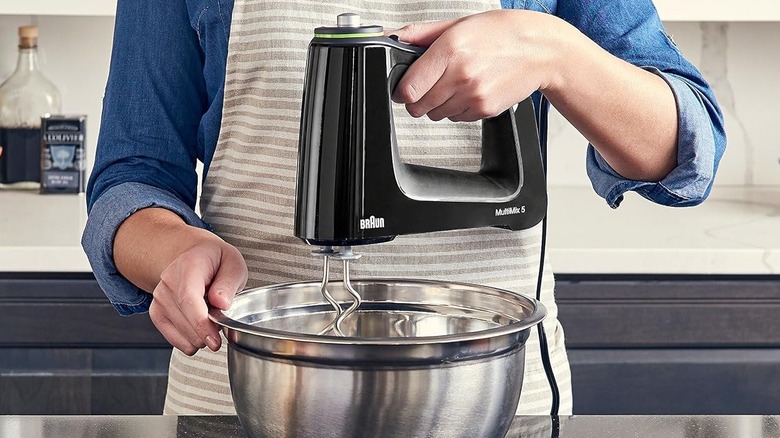 Person using a black Braun hand mixer with dough attachments.