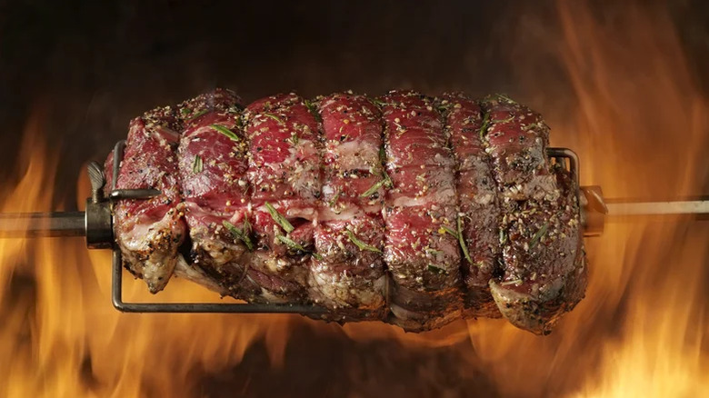 roast beef with herbs on a spit over an open fire
