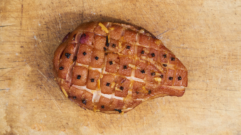 Cooked picnic ham scored and studded with cloves on wooden surface