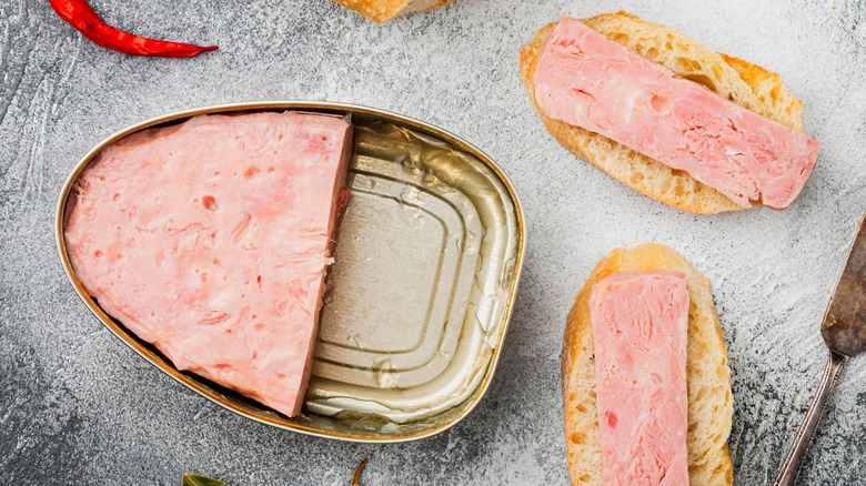 Opened tin of canned ham next to slices of ham on rounds of toast