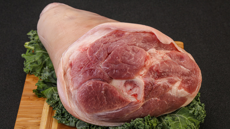 Half fresh pork leg on a bed of greens on top of wooden board