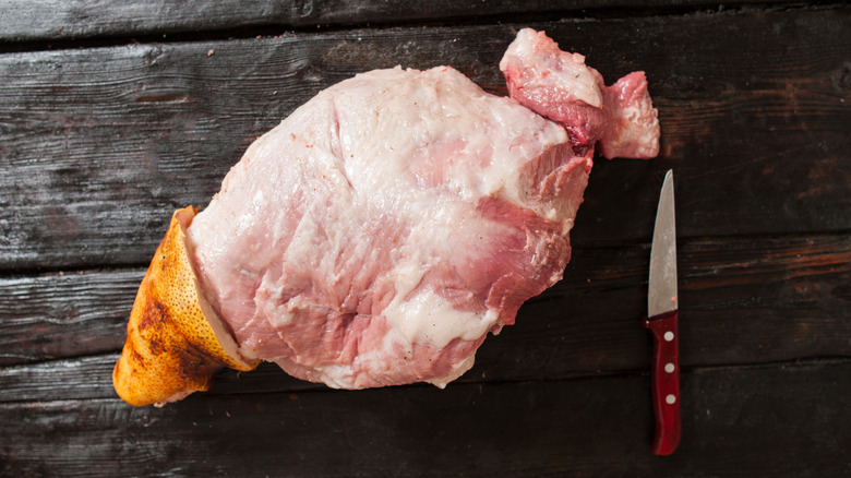 Whole fresh pork leg ham on dark wooden surface next to small paring knife