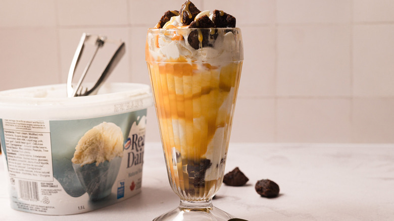 Caramel brownie sundae with large vanilla ice cream pail and a scoop