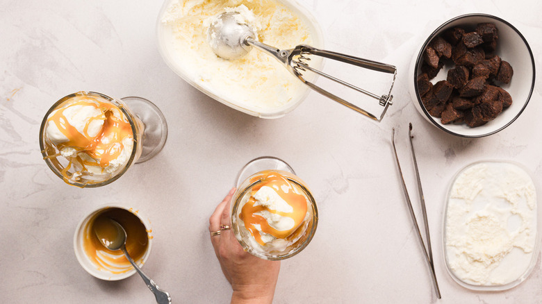 Hand holding one of two glasses with ice cream and caramel sauce