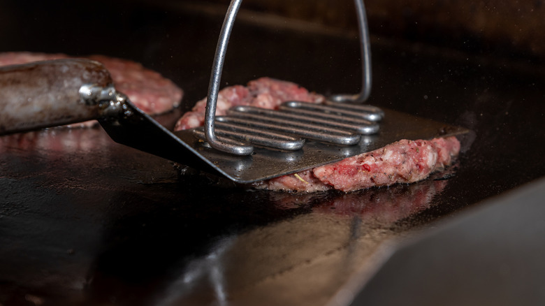 Smash burger being cooked on a grill with two spatulas