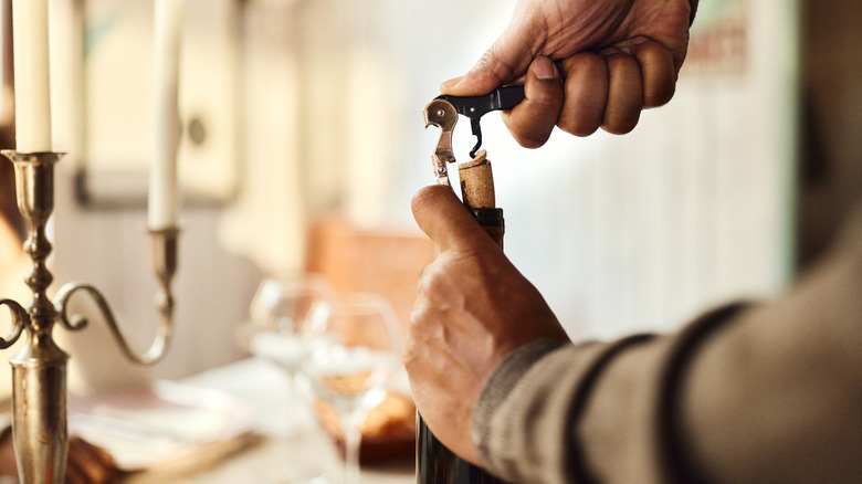 Person opening up a bottle of wine with a corkscrew