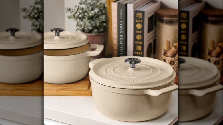 Two beige enamel Dutch ovens in front of a display of cookbooks
