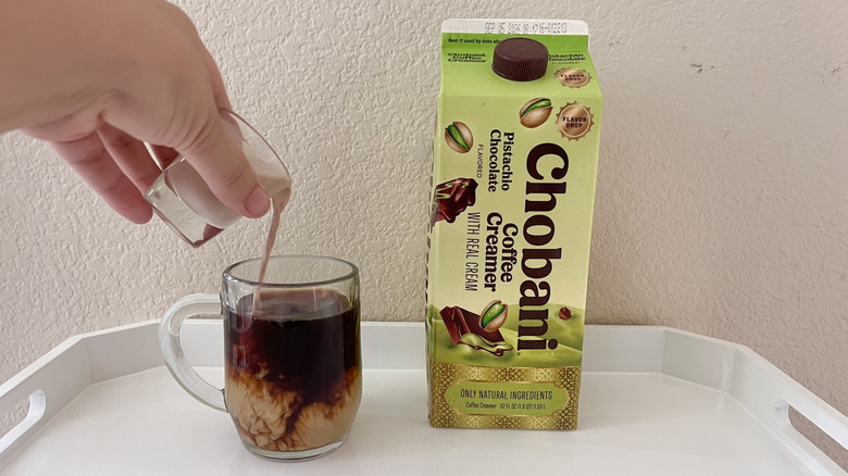 Person pouring creamer into a glass mug of coffee