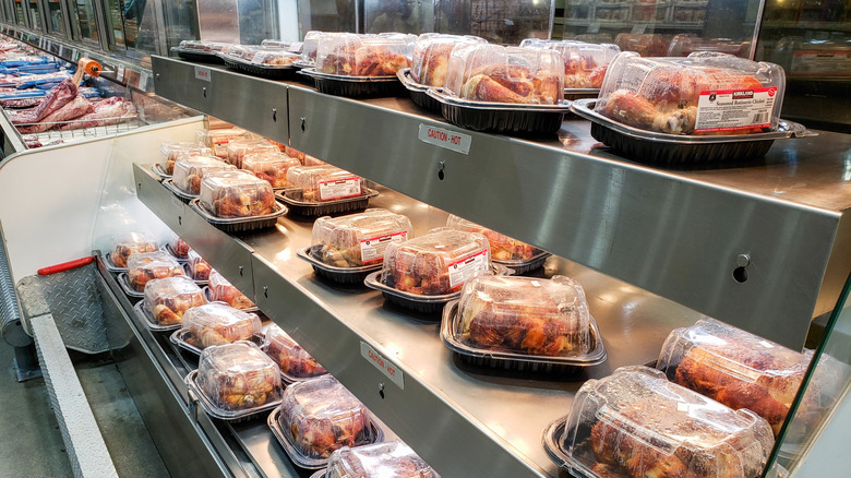 A hot food display at a Costco featuring bagged rotisserie chickens and sealed plastic trays